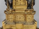 a gold clock with statues around it on a stand