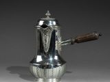 une cafetière ancienne en argent, munie d'une poignée en bois, posée sur une table
