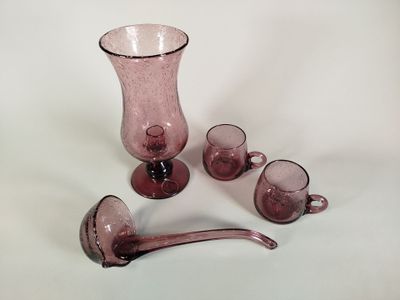 des vases et des tasses en verre violet posés sur une surface blanche, avec une cuillère