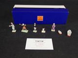 des figurines représentant divers personnages, dans une boîte bleue posée sur un fond noir
