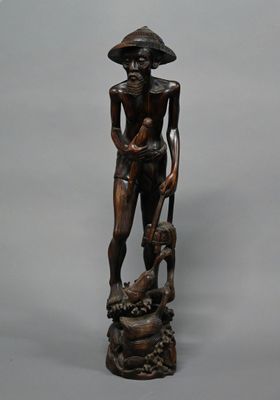 statue en bois représentant un homme coiffé d'un chapeau, accompagné d'un chien, assis sur un rocher