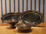 three silver dishes sitting on a table with a striped wall behind them