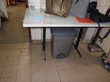 une table sur laquelle se trouve un sac, avec une poubelle devant
