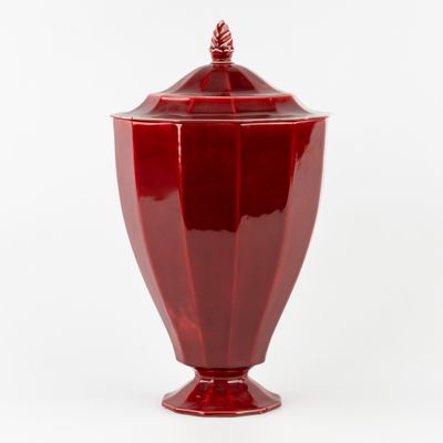 un vase rouge muni d'un couvercle, posé sur une surface blanche