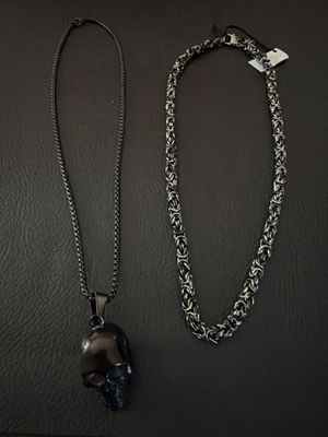 two necklaces with a skull on a chain on a black surface