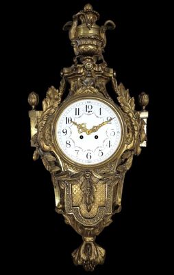 une horloge dorée surmontée d'une couronne, sur fond noir