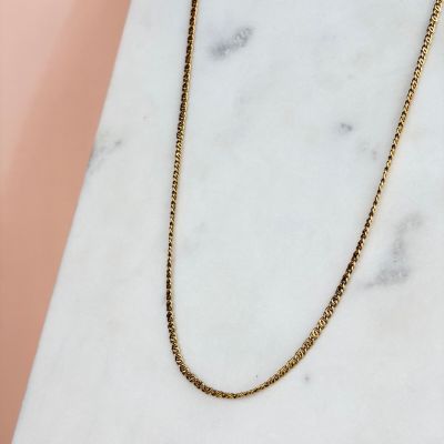un collier à chaîne en or posé sur une surface en marbre