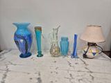 de nombreux vases de différentes couleurs posés sur une table où se trouve une lampe