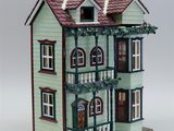 a green doll house with a red roof and a balcony