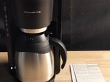 une cafetière posée sur une table en bois, à côté d'une tasse de café