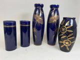 four blue vases with gold designs are lined up against a white background