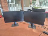 two computer monitors sitting on top of a wooden table next to each other