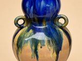 un vase bleu et vert posé sur une surface beige