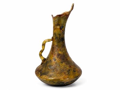 un petit vase en métal muni d'une anse torsadée, posé sur une surface blanche