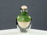 une bouteille en verre vert avec un bouchon doré, posée sur un socle blanc