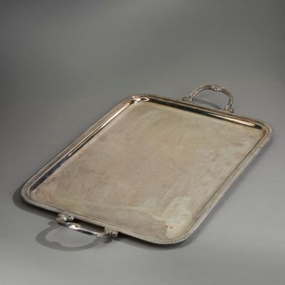 un plateau ancien en argent, muni de poignées, sur une surface grise