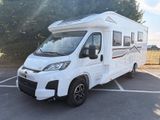 un camping-car blanc garé sur un parking, avec des arbres en arrière-plan