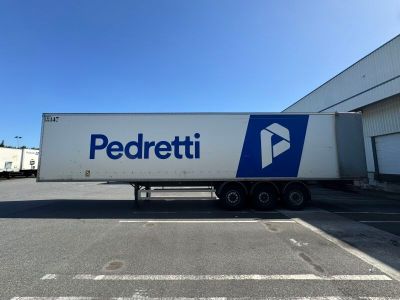 Le camion est garé devant un bâtiment sur lequel figure un logo bleu et blanc.