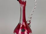 un vase en verre rouge muni d'une anse, posé sur une surface blanche