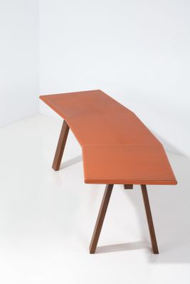 un bureau orange avec deux pieds en bois et un plateau incurvé