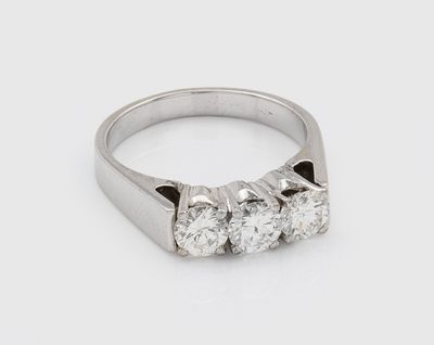 un gros plan d'une bague en diamant à trois pierres posée sur une surface blanche