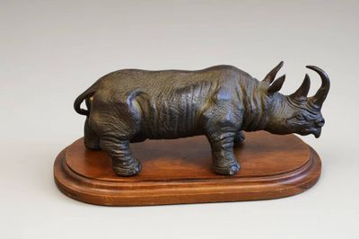 statue d'un rhinocéros posée sur un socle en bois, sur fond blanc