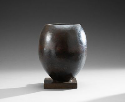 un vase noir posé sur un socle en bois, sur une surface blanche