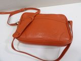 an orange leather purse with a strap on a white surface