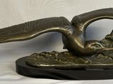 une statue en bronze représentant un oiseau, posée sur un socle noir