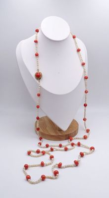 collier composé de perles de corail rouge montées sur un support en bois, sur fond blanc
