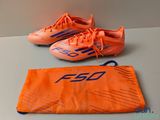 deux paires de chaussures de foot orange posées sur une table à côté d'un sac