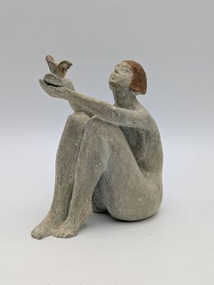statue représentant une femme assise sur une surface blanche, tenant un oiseau dans ses mains