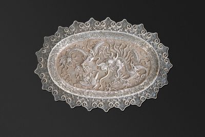 une assiette en argent ornée d'un dragon sur fond noir