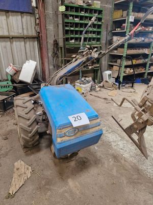 un tracteur bleu garé dans un garage, sur lequel est accrochée une pancarte