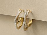 une paire de boucles d'oreilles créoles en or et diamants posée sur une feuille de papier