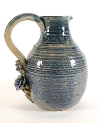 un vase bleu muni d'une anse, posé sur une surface blanche