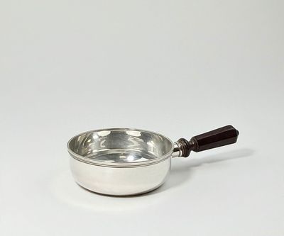 une casserole argentée avec un manche en bois posée sur une surface blanche