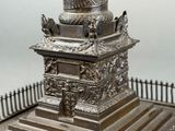 a statue of a column on a pedestal with a fence in the background