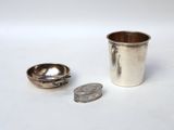 a silver cup next to a coin on a white surface