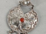a close up of a silver pendant with a red stone on it