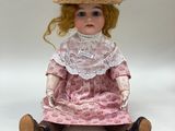 doll sitting on a white surface wearing a pink dress and a straw hat