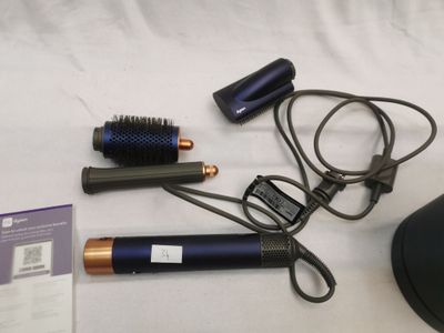 une photo montrant un sèche-cheveux, une brosse et d'autres objets disposés sur un lit