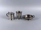 trois tasses en métal argenté et une soucoupe posées sur une table