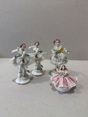 trois figurines en porcelaine représentant des femmes en robe, accompagnées de fleurs posées sur une table
