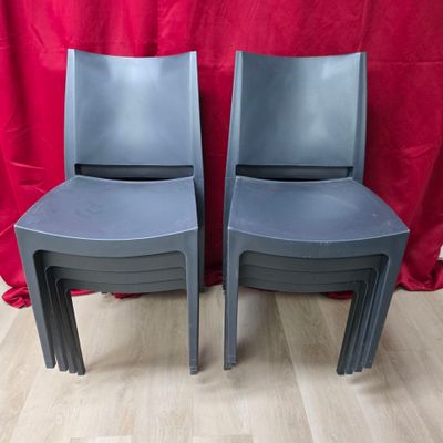 deux chaises en plastique grises posées sur un parquet, à côté d'un rideau rouge