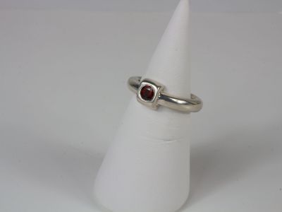 silver ring with garnett stone on top of a white cone