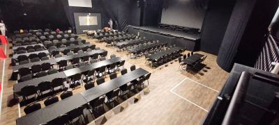 un grand auditorium équipé de tables et de chaises ainsi que d'un écran de projection