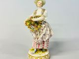 an antique porcelain figurine of a woman holding a basket of flowers