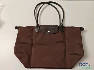 Le sac Longchamp est marron et possède une poignée noire.