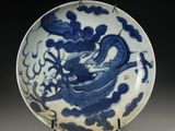 blue and white plate with a dragon on it on a stand